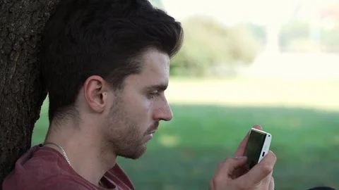 Absorbed man leaning on a tree and texting messages on smartphone Stock-Footage 69965870