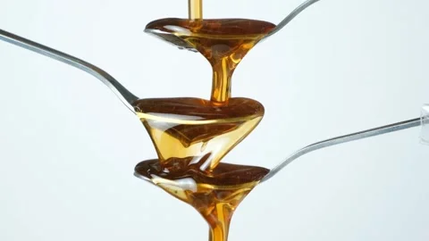 Abstract art of maple syrup flowing over spoons, slow motion on white background Stock Footage 336907189