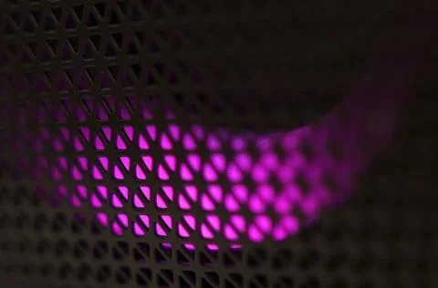 Abstract background of a black patterned lattice behind which purple LEDs glo Stock Photos