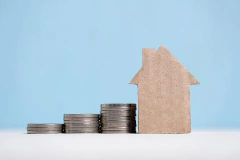 Abstract cardboard house next to a stack of coins. Real estate savings concep Stock Photos