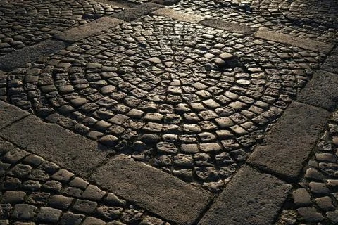 Abstract cobblestone pavement pattern with circular stone design illuminated by Stock Photos