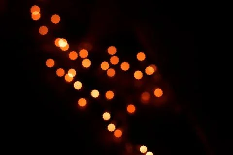 Abstract dark background with glowing orange bokeh light spots shaping a fe.. Stock Photos