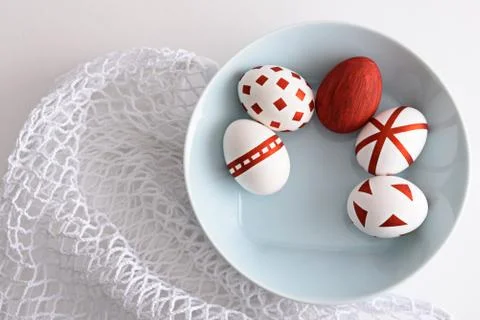 Abstract Easter eggs with red geometric patterns in blue plate on white mesh  Stock Photos
