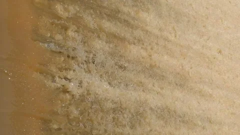 Abstract of fast-flowing, yellowish-brown water foaming and frothing as it .. Video stock 322557600