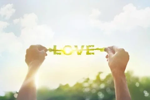 Abstract, hands holding a green leaf with word LOVE on vibrant cloudy sky Fotos de archivo
