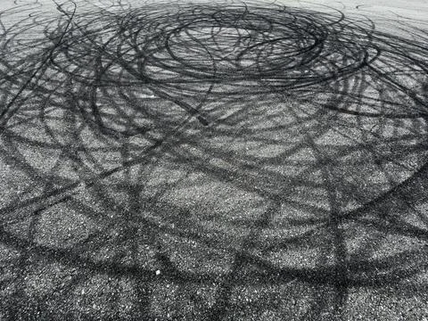 Abstract pattern of dark, swirling tire marks on a textured asphalt surface Stock Photos