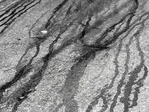 Abstract patterns of dark streaks on textured, grayish ground surface Stock Photos