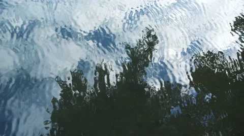 Abstract reflection in rippling water of cloudy sky and tree overhead Stock Footage 67343279