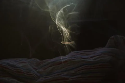 Abstract smoke rising from a textile surface in a dark room setting Stock Photos