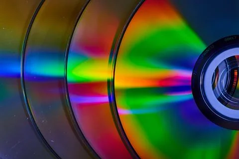 Abstract stack of four CDs with reflective rainbow bursts of light on surface Stock Photos