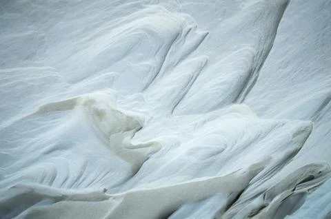 Abstract texture of white snow and wind-sculpted sand dunes. Stock Photos