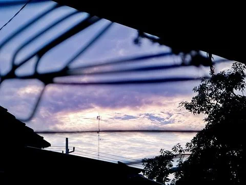 Abstract view of a cloudy sky framed by a wire mesh fence, with a cell towe.. Stock Photos