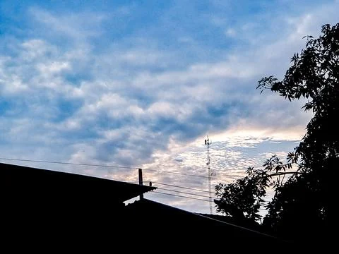 Abstract view of a cloudy sky framed by a wire mesh fence, with a cell towe.. Stock Photos
