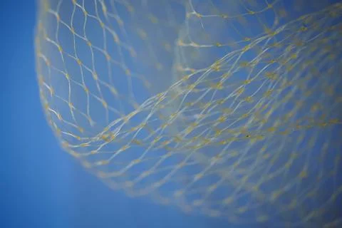 Abstract wave of yellow nylon mesh against a bright blue sky. Close-up of dec Stock Photos