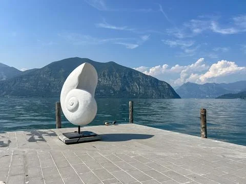 Abstract White Snail Shell Sculpture on a Stone Dock by a Calm Lake Stock Photos