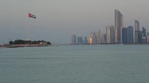 Abu Dhabi skyline with UAE flagpole on Marina Island, reflecting sunset Stockbeeldmateriaal 331342869