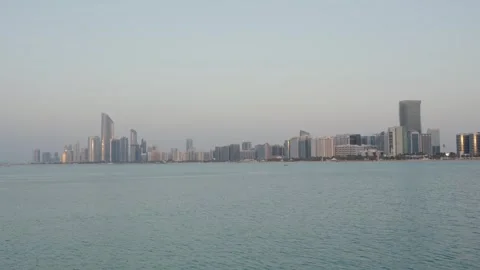 Abu Dhabi skyline with UAE flagpole on Marina Island, reflecting sunset Видео 331343602