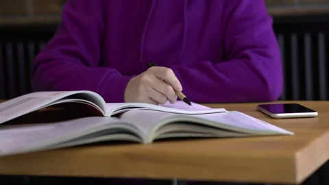 Academic pursuits student sits at table with phone books and notes making notes Stock Footage 277772848