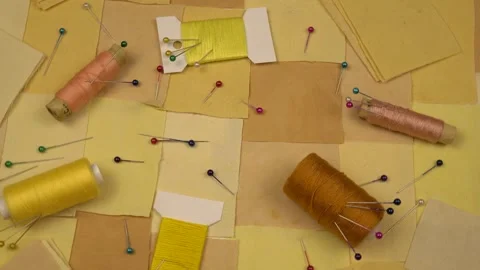 Accessories for patchwork sewing lie on a patchwork textile in yellow tones Stock Footage 260640277
