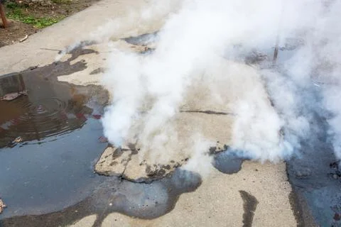 Accident on heating systems. White steam comes out of cracks in the asphalt. Stock Photos