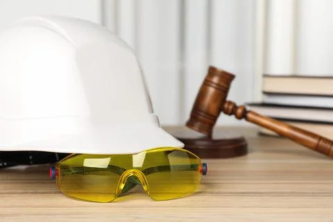 Accident at work. Goggles, hardhat and gavel on wooden table, selective focus Stock Photos