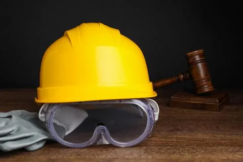 Accident at work. Hardhat, goggles, gloves and gavel on wooden table, closeup Stock Photos