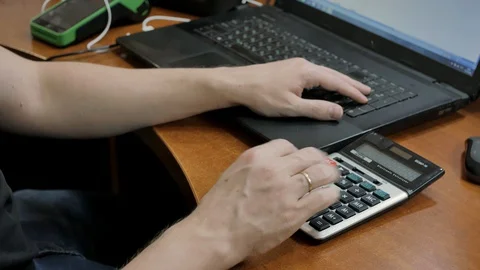 The accountant at home at the computer counts the numbers on the calculator and Stock Footage 128142763