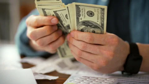 Accountant sits at a table counting cash while consulting documents and a ca Stock Footage 336570452