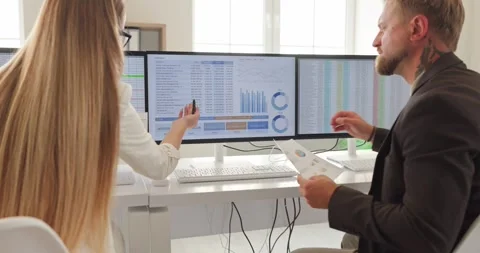 Accountants review data on multiple monitors in office, discussing reports Stock Footage 345738170