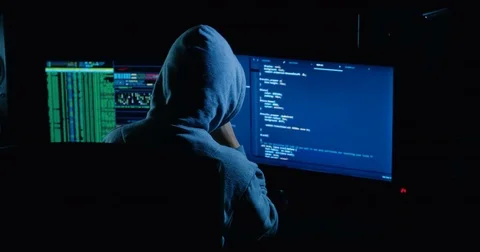 Acker in hood cracking code using laptop and computers from his dark hacker room Stock Footage 82916262