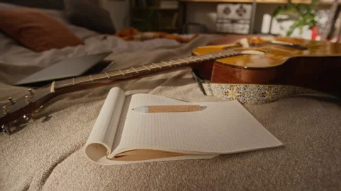 Acoustic Guitar and Open Notebook Resting on Bed for Songwriting Stock Footage 337496008