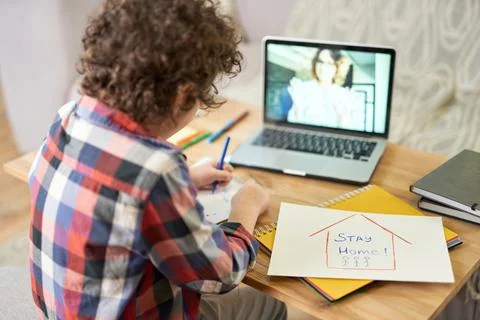Acquiring knowledge. Rear view of hispanic school boy drawing Stay Home sign Stock Photos