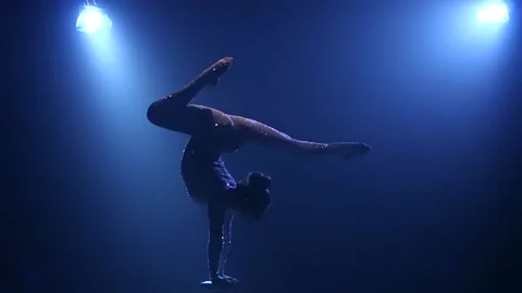 Acrobat girl on stage does acrobatic stunts standing on hands . Smoke blue Stock Footage 101776618