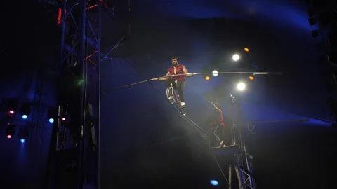 An acrobat rides a bicycle on a tightrope under the dome of the circus. Stock Footage 309084873