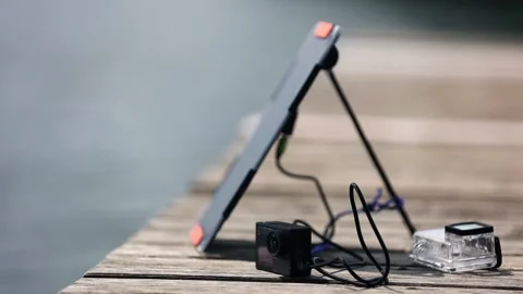An action camera is charged from a small solar panel at the wooden pier. Stock Footage 157789185