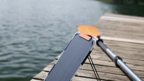 An action camera is charged from a small solar panel at the wooden pier. Vídeo Stock 157789408