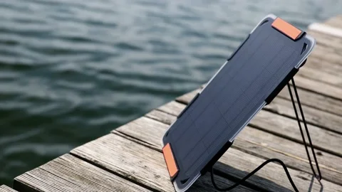 An action camera is charged from a small solar panel at the wooden pier. Stock Footage 157789486