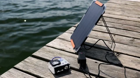 An action camera is charged from a small solar panel at the wooden pier. Stock Footage 157789578