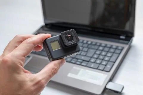 Action camera in hand. Laptop in background. Concept of transferring and stor Stock Photos
