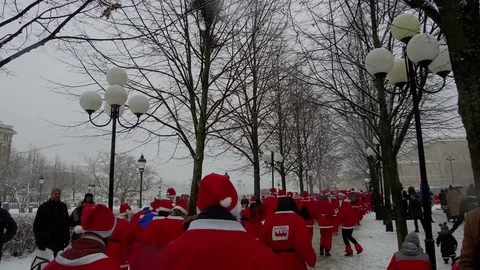 Action camera moves smoothly behind crowd of Santa Clauses running for new year Stock Footage 70633374