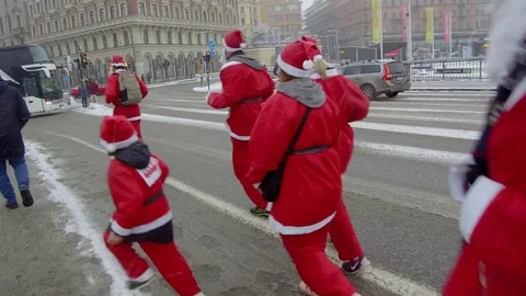 Action camera moves smoothly behind crowd of Santa Clauses running in street Stock Footage 70633972