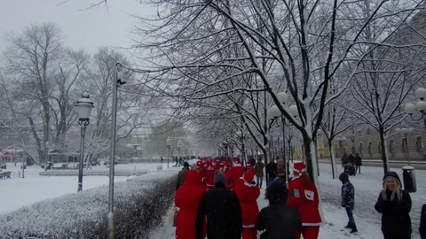 Action camera moves smoothly behind crowd of Santa Clauses running heavy snow Video stock 70634076