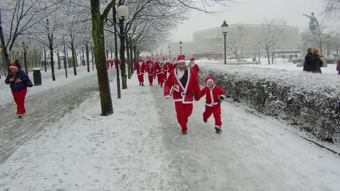 Action camera moves smoothly toward crowd of Santa Clauses running in heavy snow Video stock 70633845