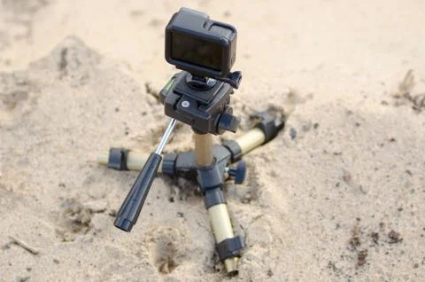Action camera stands on a small tripod, recording video on a sandy beach. Stock Photos
