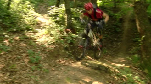 Action shot of two pro downhill cyclists jumping over a log the woods Stock Footage 55916135