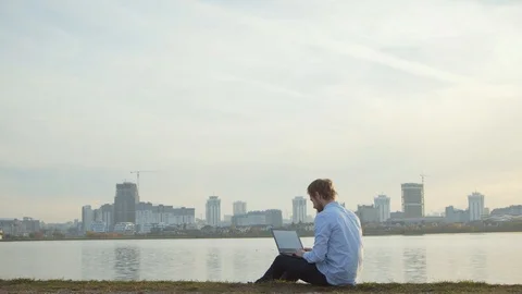 Active and mobile young man with laptop sitting on the lake Stock Footage 99388305