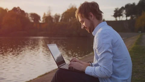 Active and mobile young man with laptop sitting on the lake Stock Footage 99836827