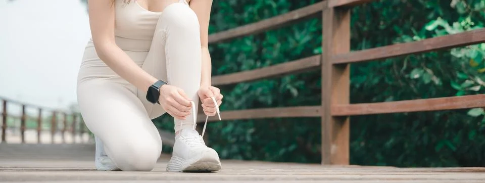 Active athlete runner tying white sneaker shoelace on wooden bridge during .. Stock Photos