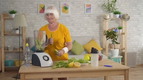 Active athletic elderly woman throws celery in the blender and makes a smoothie Stock Footage 114357672