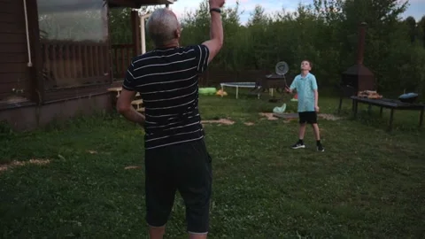 Active boy play badminton with cheerful grandfather outdoors in the courtyard of Stock Footage 208681599
